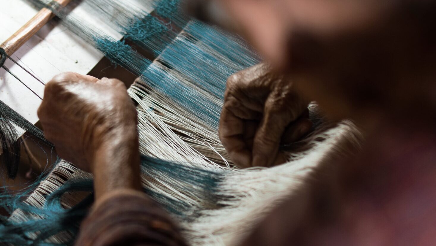 Hands weaving silk threads on a traditional loom